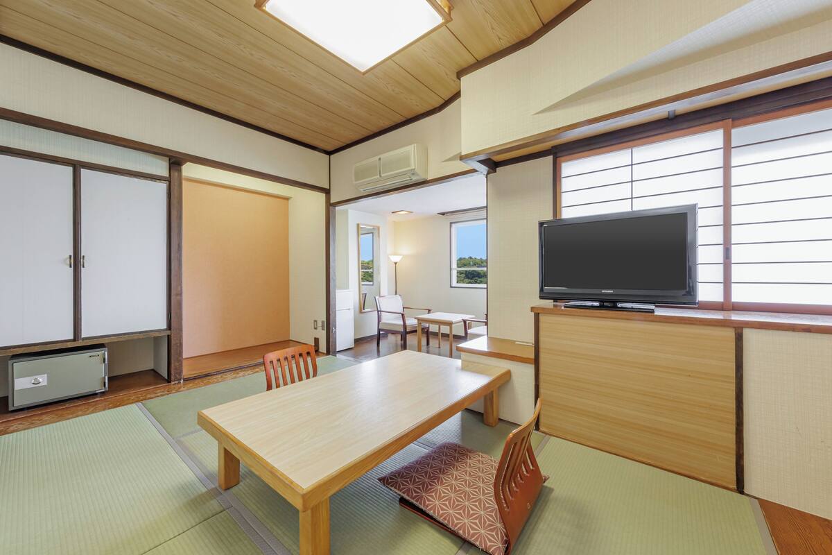 A traditional Japanese room with tatami flooring, a low wooden table, a television, and sliding doors.