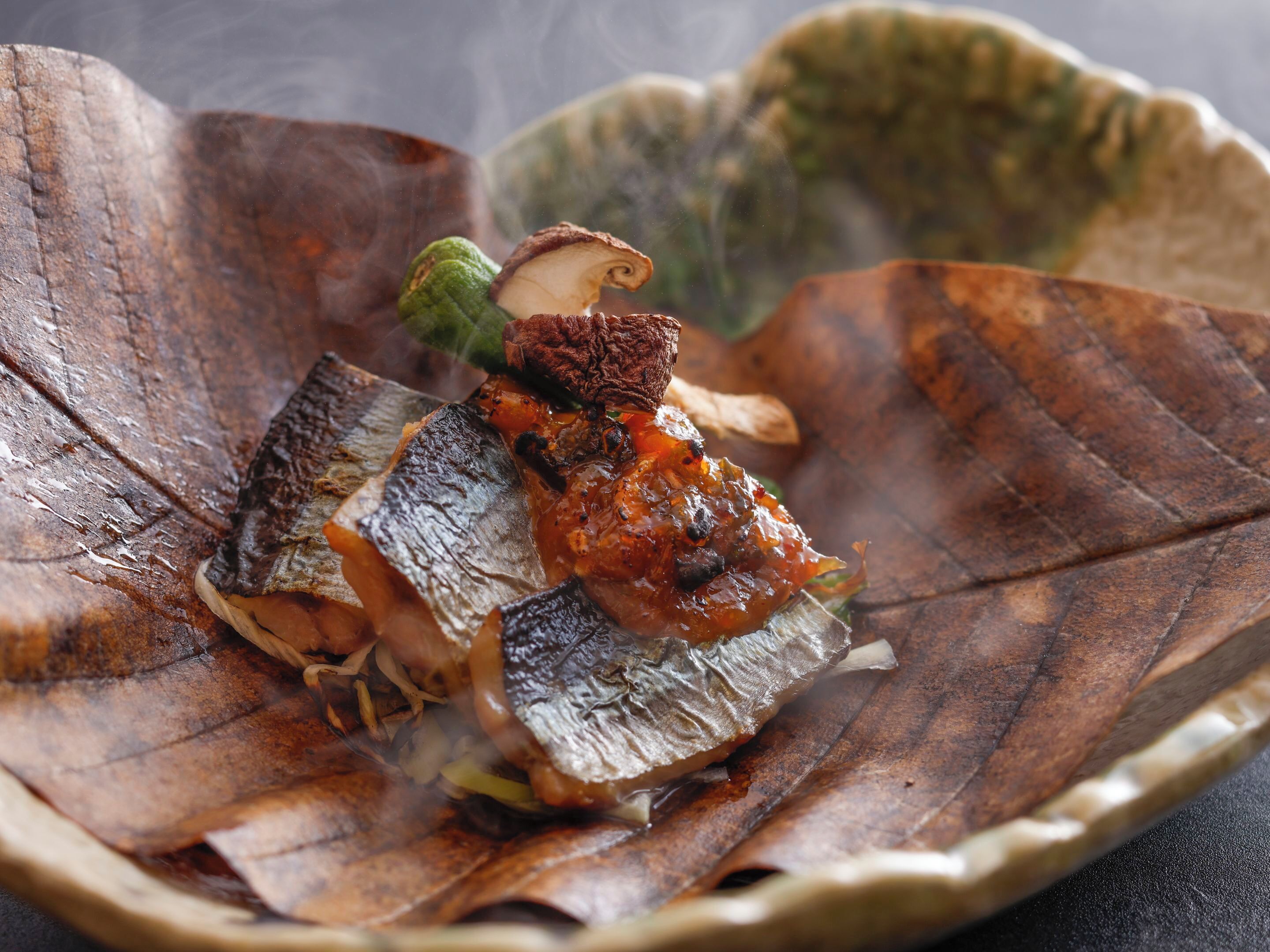 A dish with grilled fish and vegetables on a leaf-shaped plate.