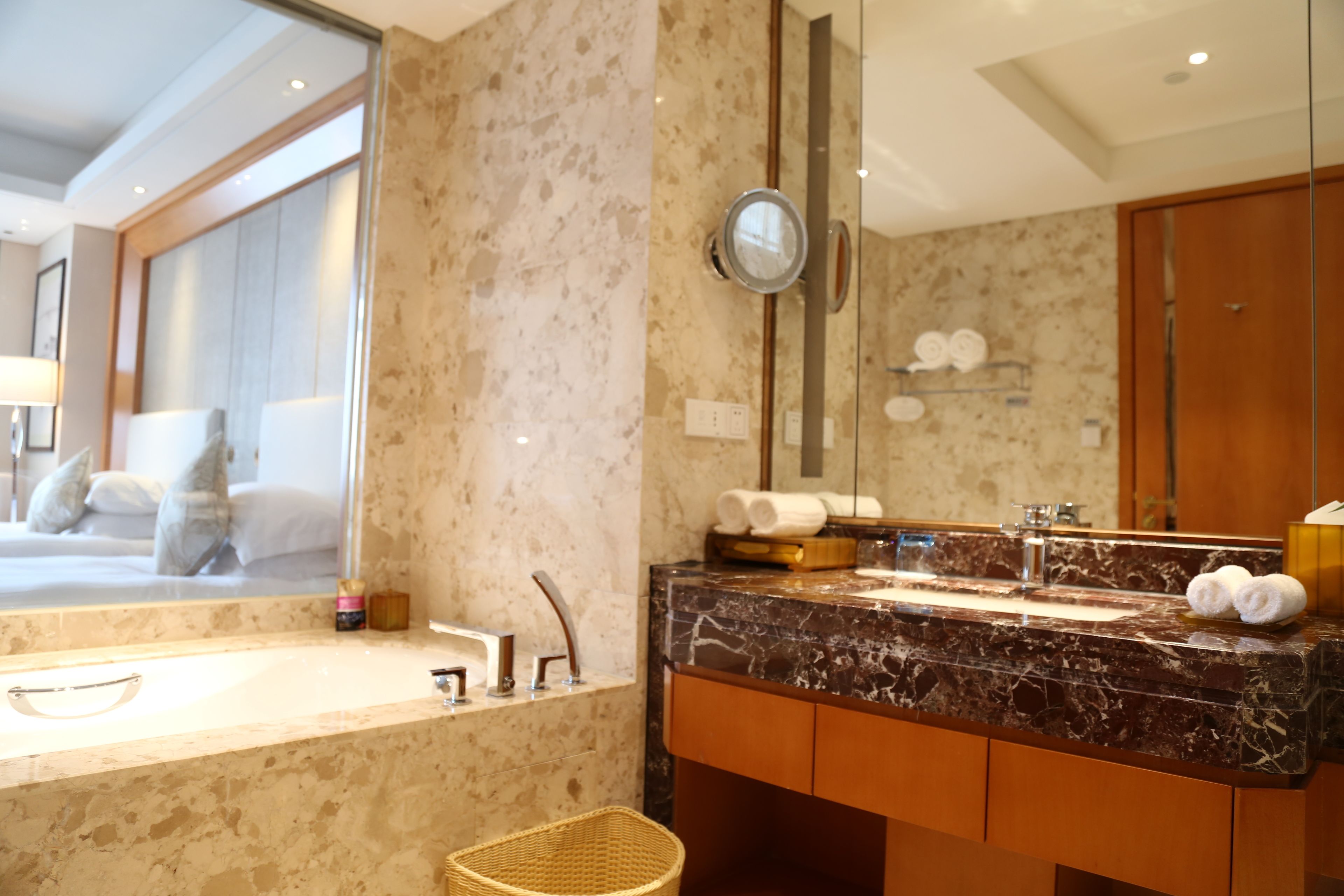 A modern bathroom with a marble sink, a large mirror, and a view of a bedroom.