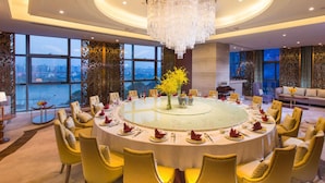 Une table de salle à manger ronde, entourée de chaises jaunes, un lustre et une vue sur la ville grâce à de grandes fenêtres.