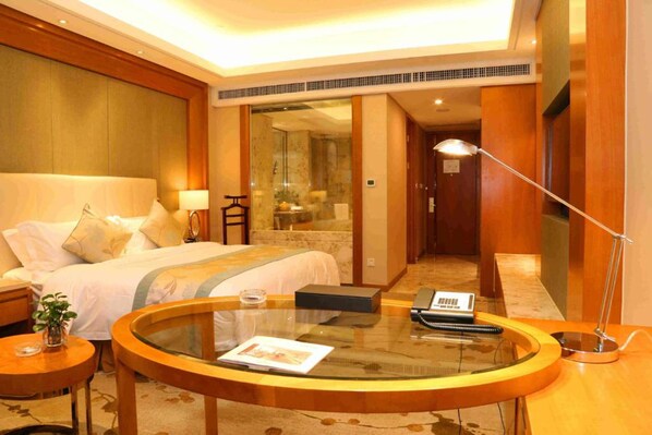 Een hotelkamer met een bed, een glazen bijzettafeltje, een nachtkastje met een lamp en een telefoon.