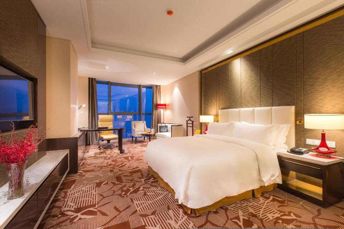 Ein Hotelzimmer mit einem großen Bett, einem Schreibtisch mit Stuhl, einem Fernseher und einem Fenster mit Blick.