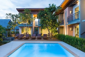 Un hotel moderno con piscina, mobiliario exterior y abundante vegetación.