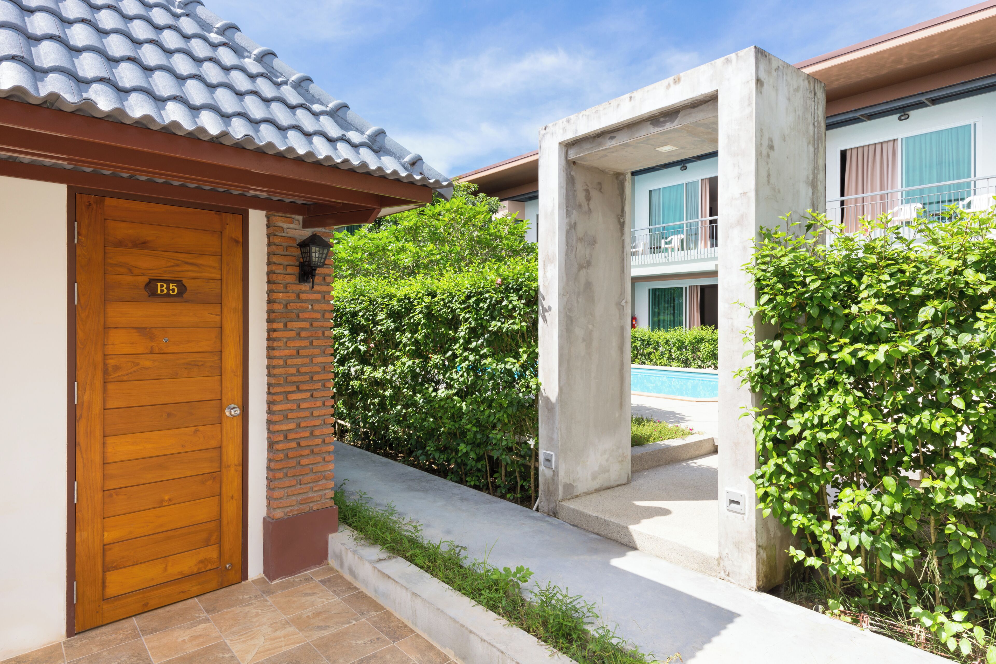 Una puerta de madera con una placa con un número, un muro de ladrillo, una estructura de concreto y una piscina al fondo.