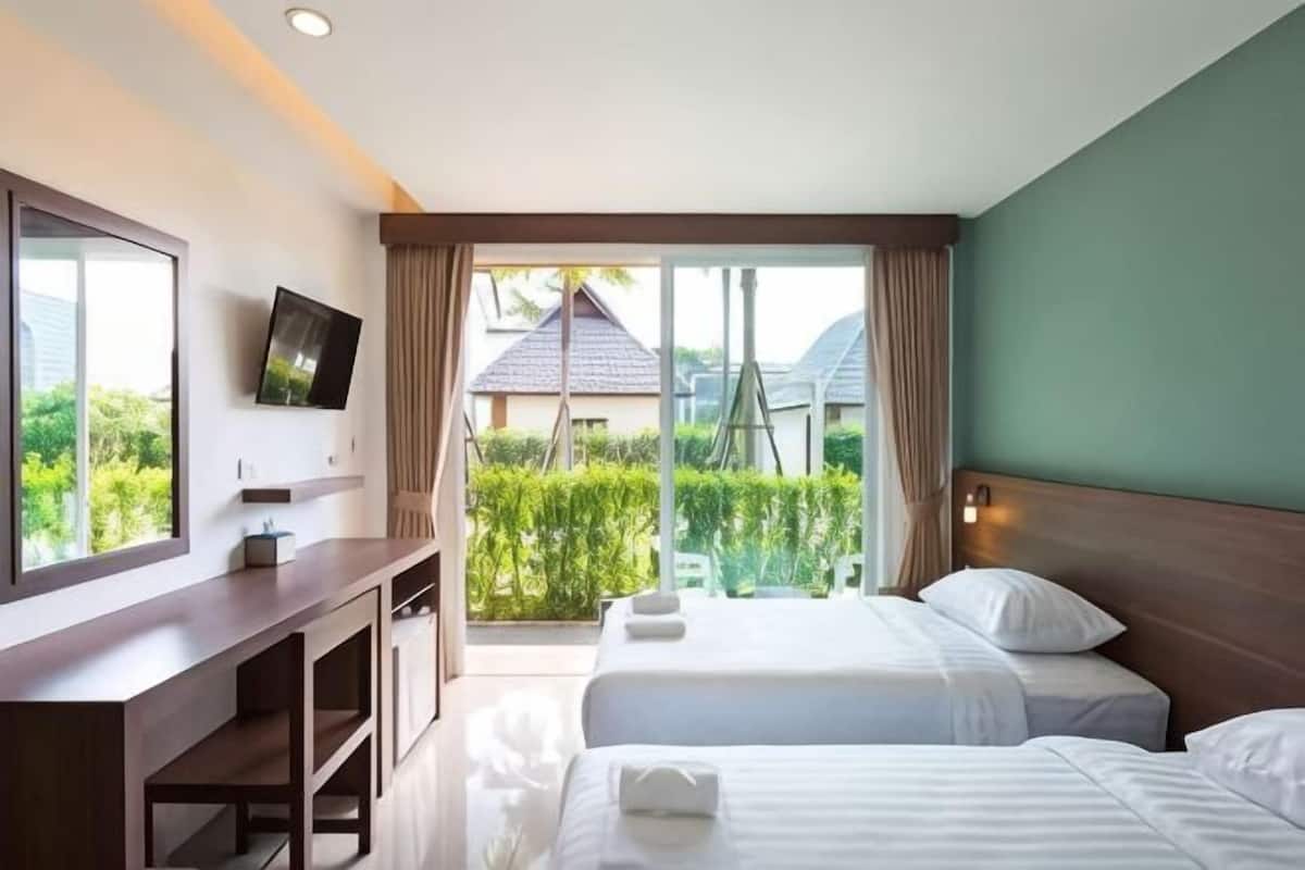 Habitación de hotel con dos camas, televisión, escritorio y ventana grande con vistas a zonas verdes y edificios.