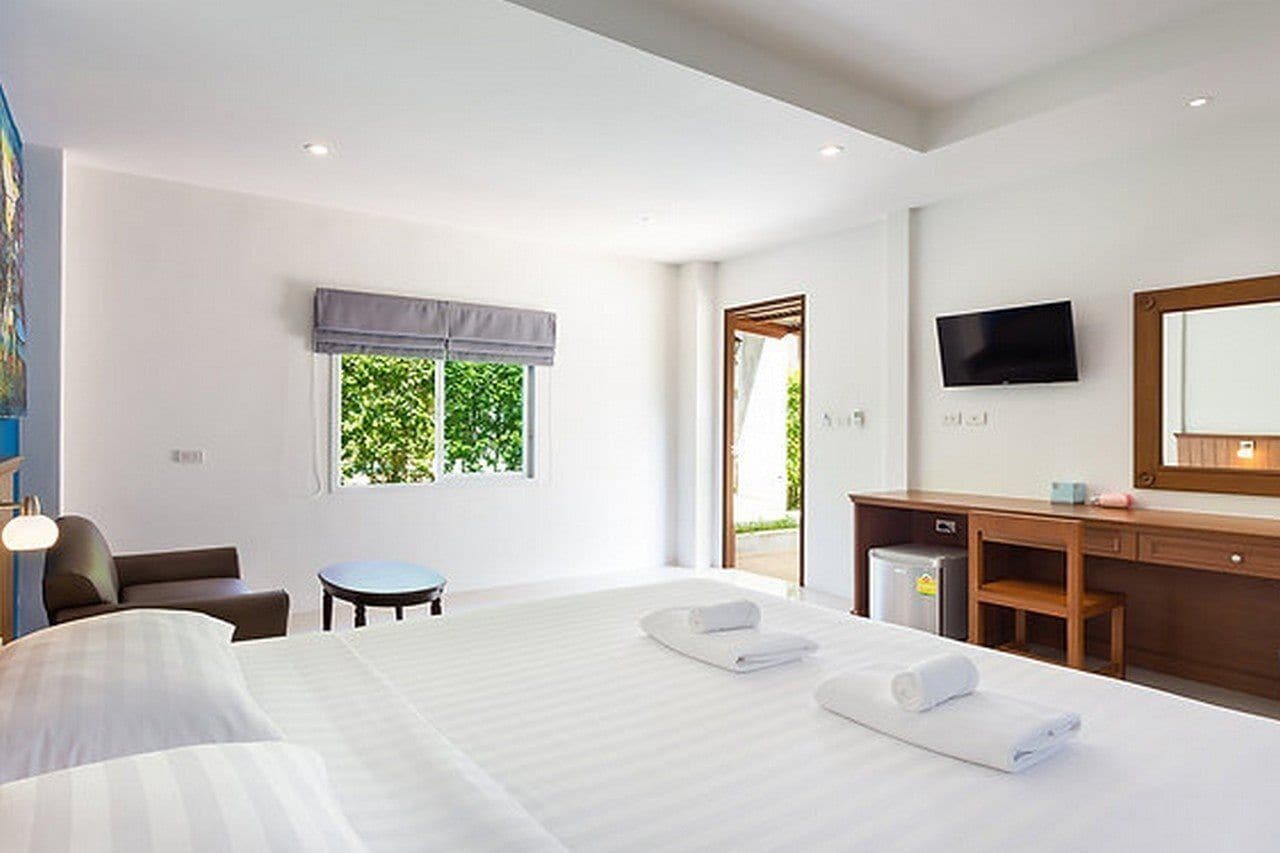 A hotel room with a large bed, a desk, a chair, a television, and a window with a view of greenery.