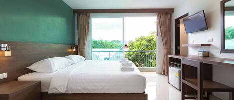 Habitación de hotel con cama, escritorio, televisión y balcón con vistas a zonas verdes.