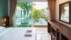 A hotel room with a bed, a desk, a chair, and a balcony with a view of greenery and buildings. - Parida Resort (Choeng Thale)