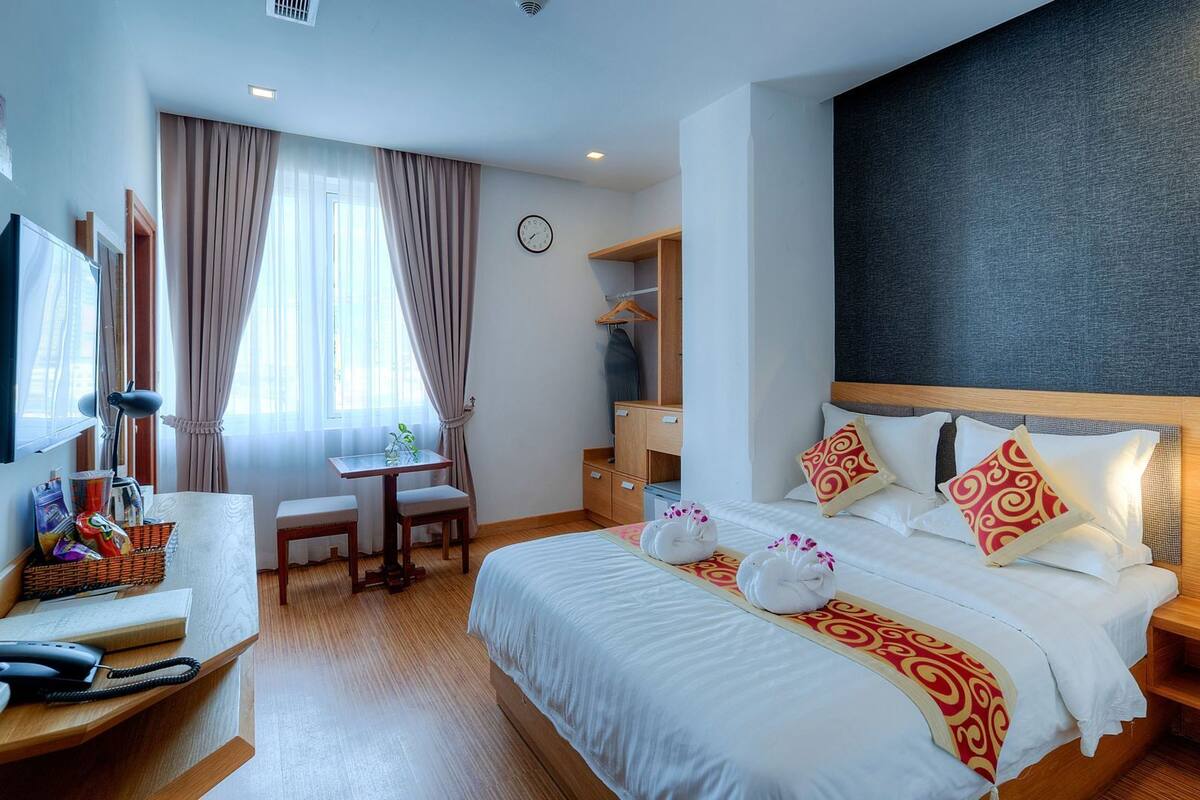 Ein Hotelzimmer mit Bett, Nachttisch, Schreibtisch, Stuhl und einem großen Fenster mit Vorhängen.