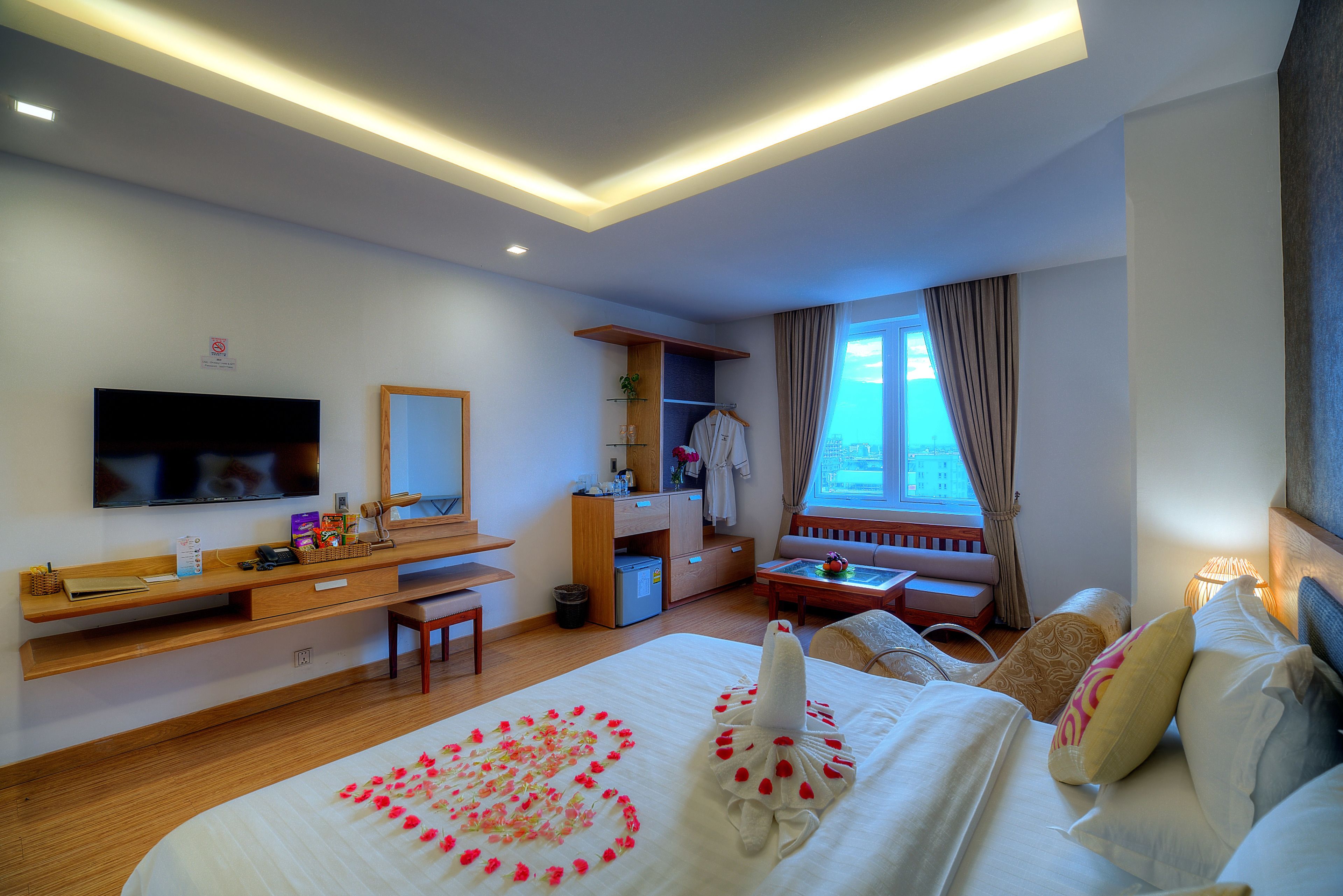 A hotel room with a bed, a desk, a television, a window with curtains, and a sofa.