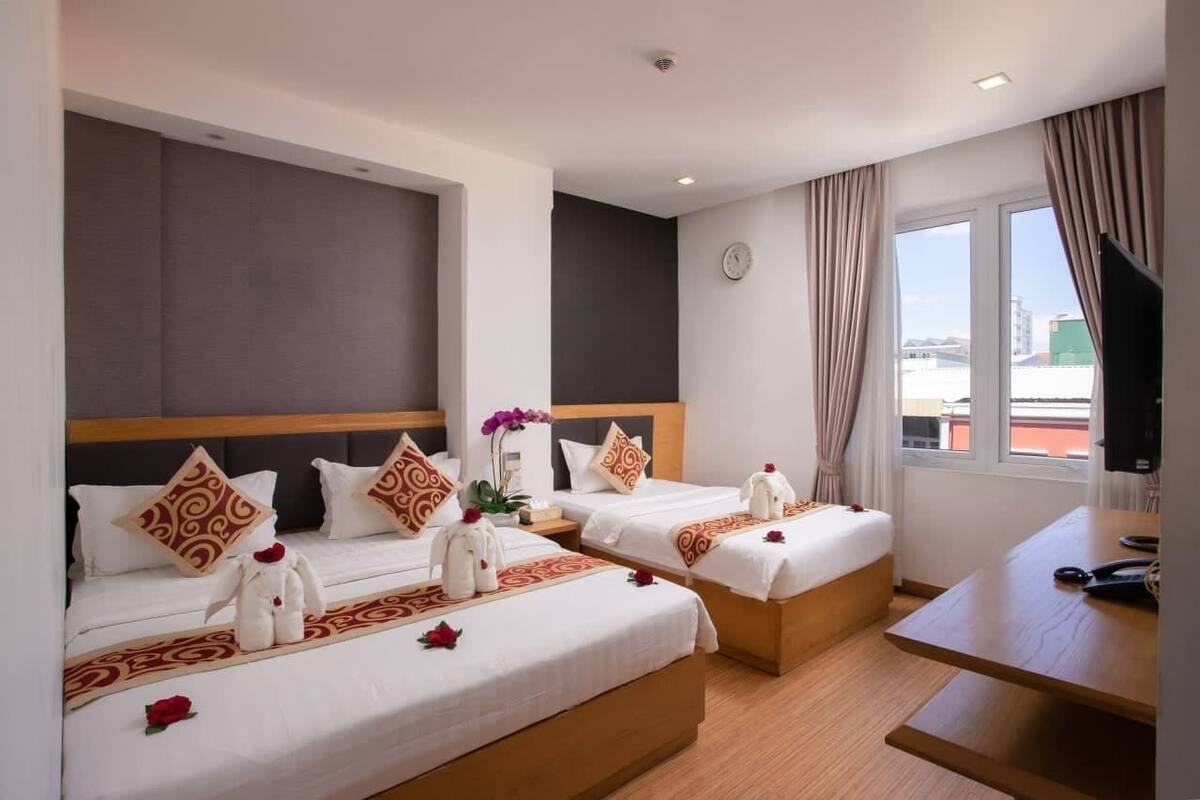 Ein Hotelzimmer mit zwei Betten, einem Schreibtisch, einem Fernseher und einem Fenster mit Blick auf die Stadt.