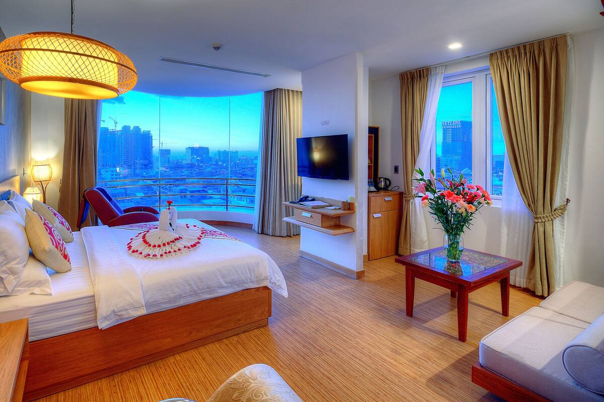 Ein Hotelzimmer mit Bett, Fernseher, Schreibtisch, Stuhl und Blick auf die Stadt.