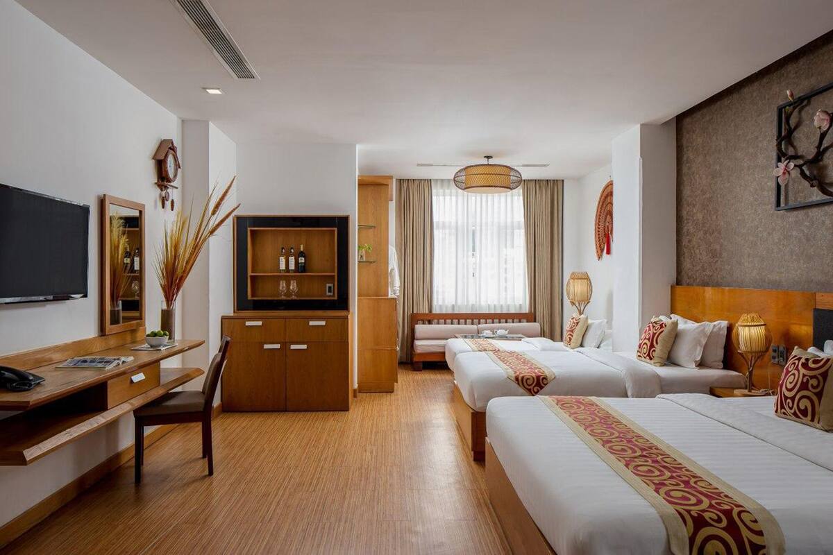 Ein Hotelzimmer mit Schreibtisch aus Holz, Fernseher, Minibar, einem Bett mit zwei Kissen und einem großen Fenster mit Vorhängen.
