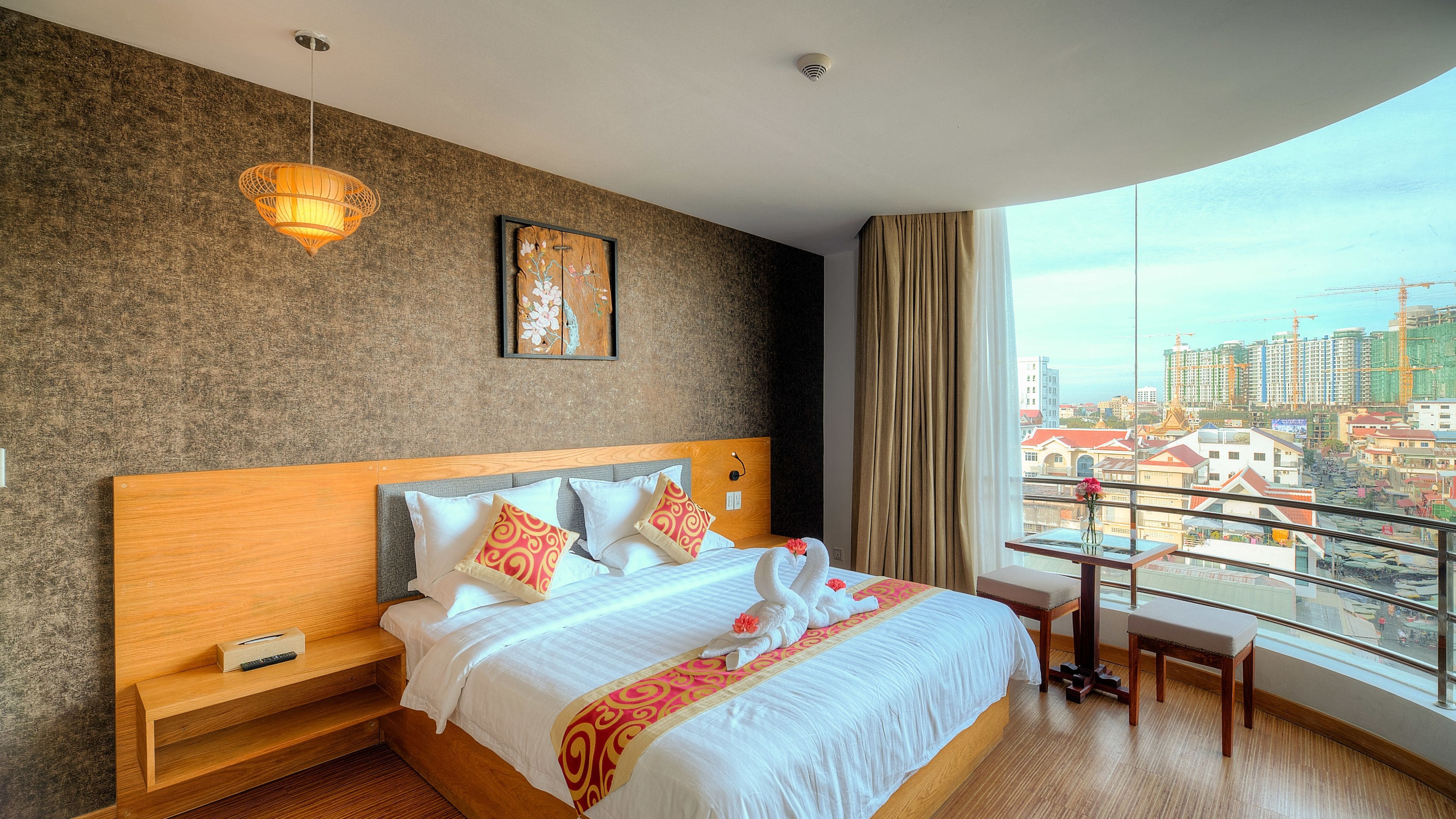 A hotel room with a large bed, wooden headboard, and a view of a cityscape through a large window.