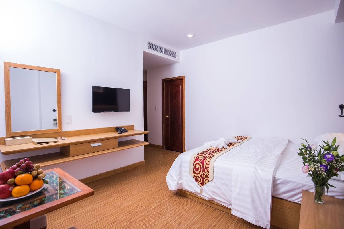 Ein Hotelzimmer mit Bett, Fernseher, Schreibtisch aus Holz und Spiegel.