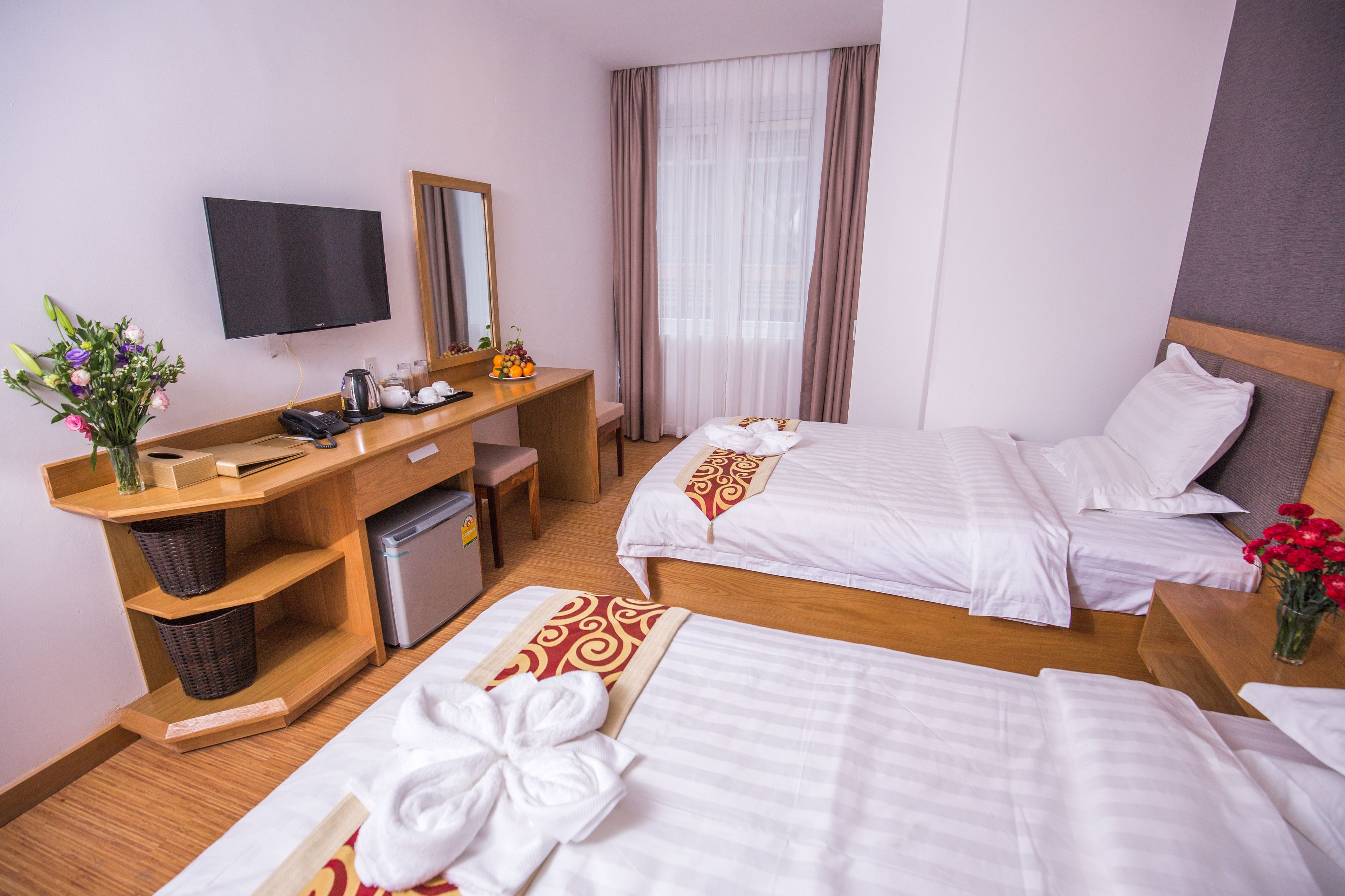 Habitación de hotel con dos camas, un escritorio, un televisor de pantalla plana, cafetera y un refrigerador pequeño.