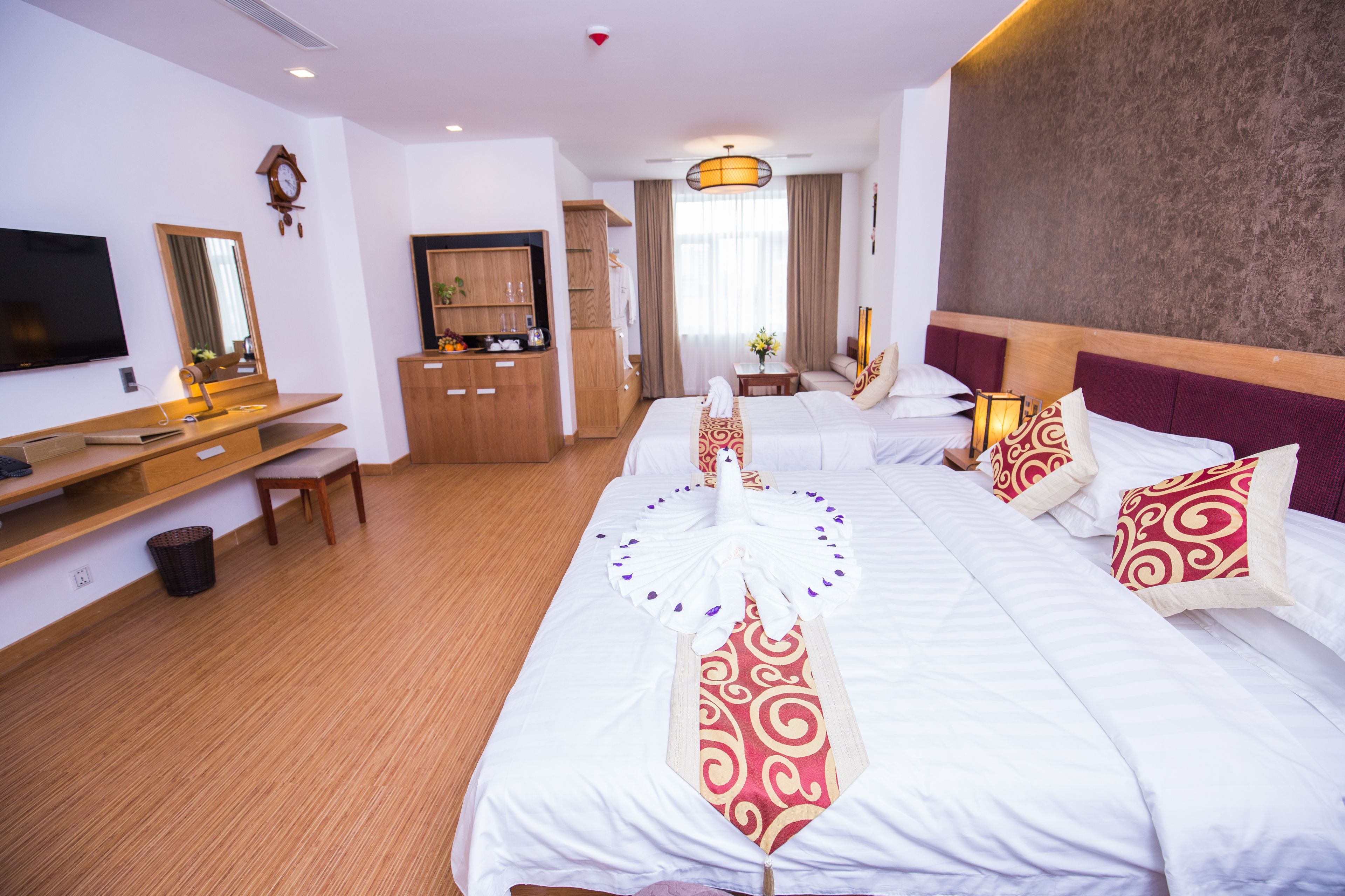 A hotel room with a large bed, a desk with a chair, a television, and a wardrobe.