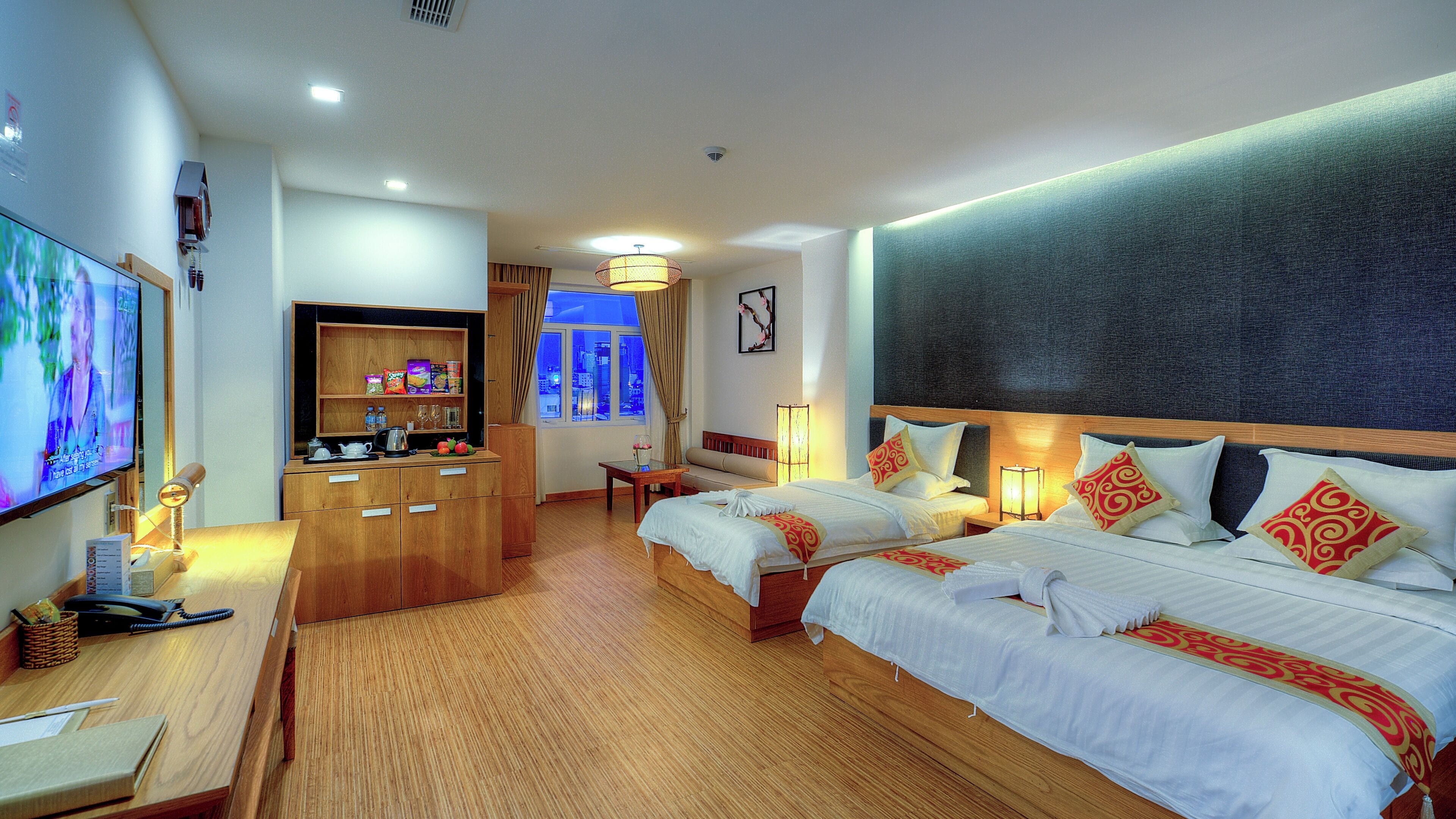 A hotel room with two beds, a TV, a desk, and a view of the city.