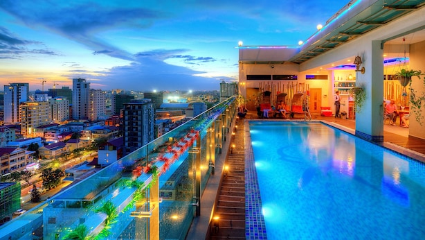 Piscina infinita en la azotea con vistas a la ciudad, barandillas de vidrio e iluminación ambiental.