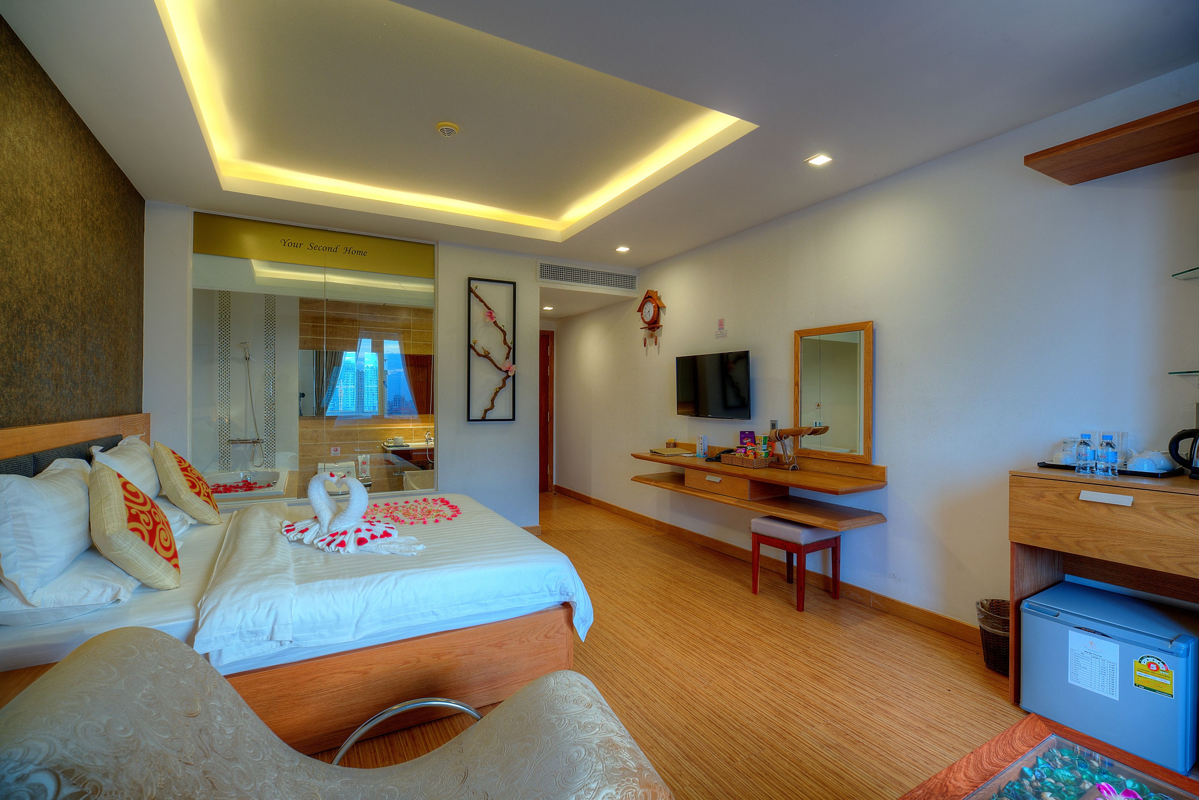 A hotel room with a bed, a desk, a mirror, a television, and a small refrigerator.
