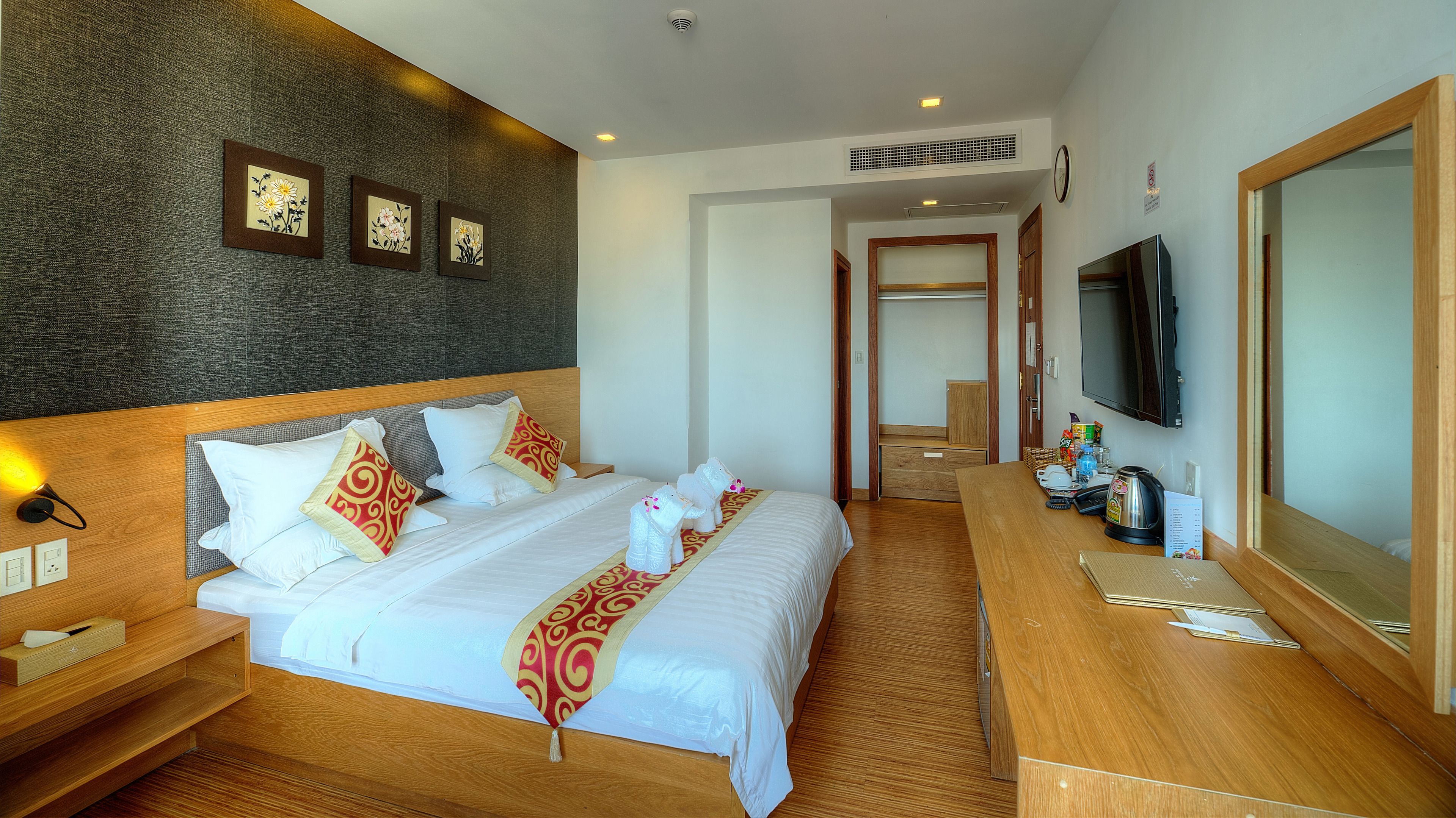 A hotel room with a large bed, wooden headboard, a flat-screen TV, a wooden dresser, and a small desk.