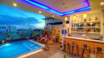 A rooftop bar with a pool, bar stools, and a city view.