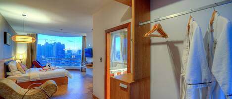 Una habitación de hotel moderna con cama, zona de estar, televisor y vista a la ciudad.