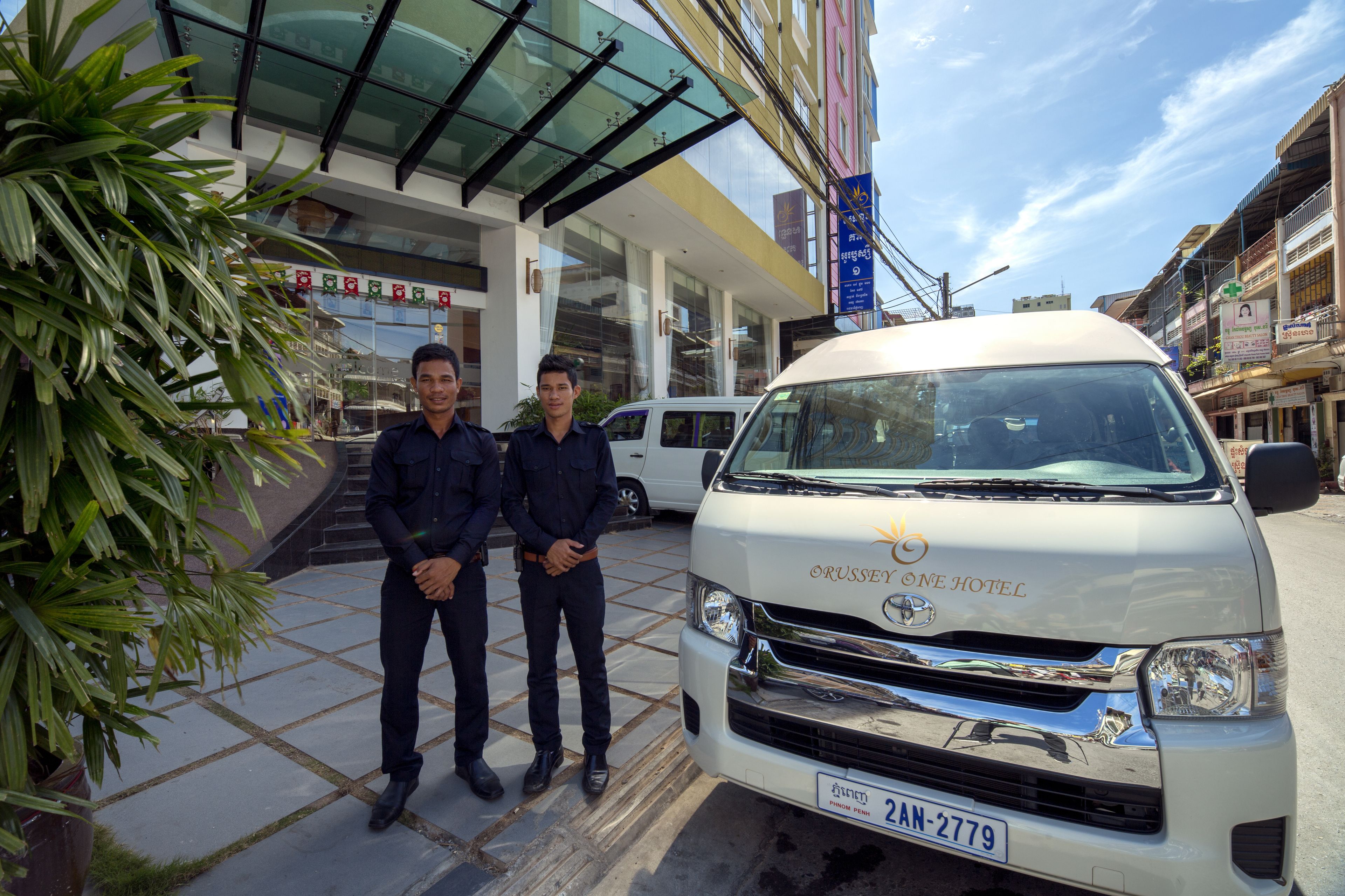 Two men standing in front of a white van with the text "ORUSSEY ONE HOTEL" on the front.