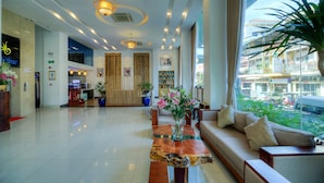 Un hall de hotel con mostrador de recepción, zona de estar y grandes ventanales con vistas a la calle.