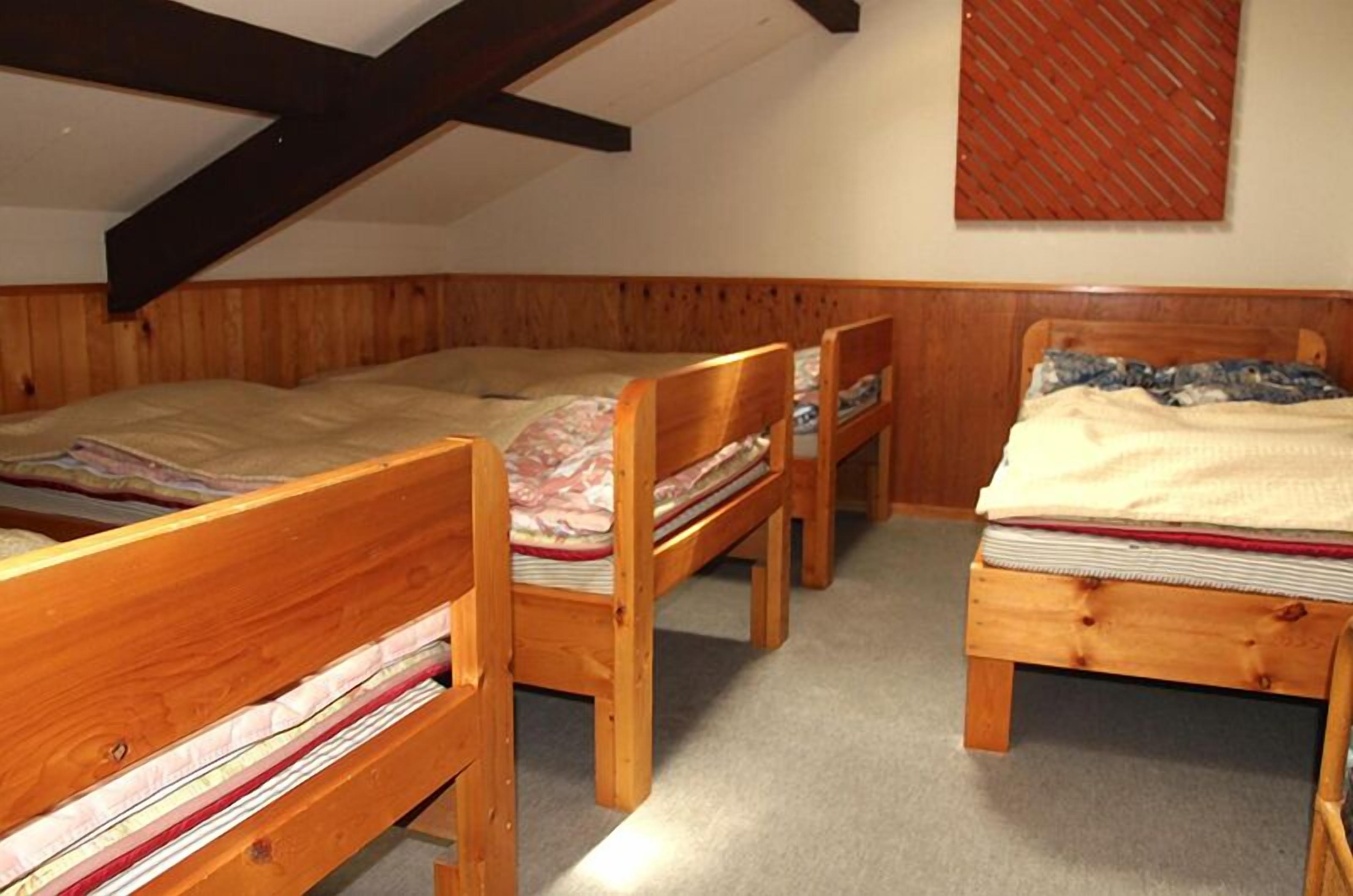 A dormitory room with three wooden bunk beds arranged in a row.