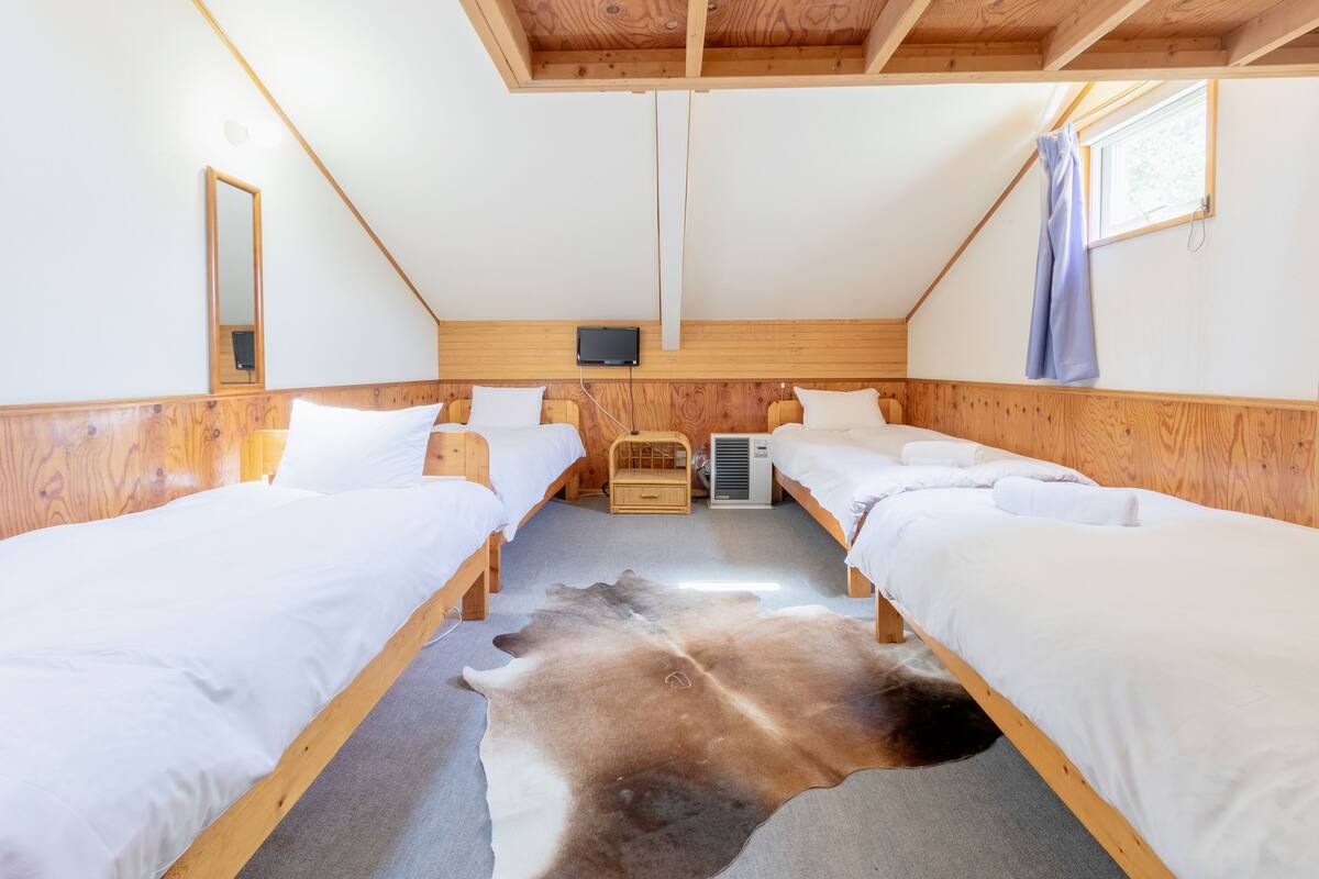 A room with two wooden beds, a large fur rug, a wooden wall panel, a mirror, and a small wooden chest.
