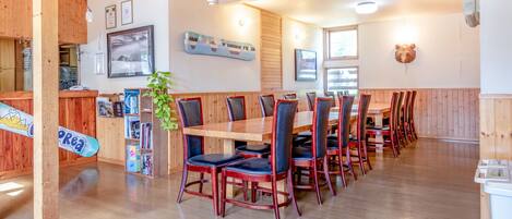 A restaurant with wooden walls and a long dining table with chairs. There is a counter with a menu and a plant.