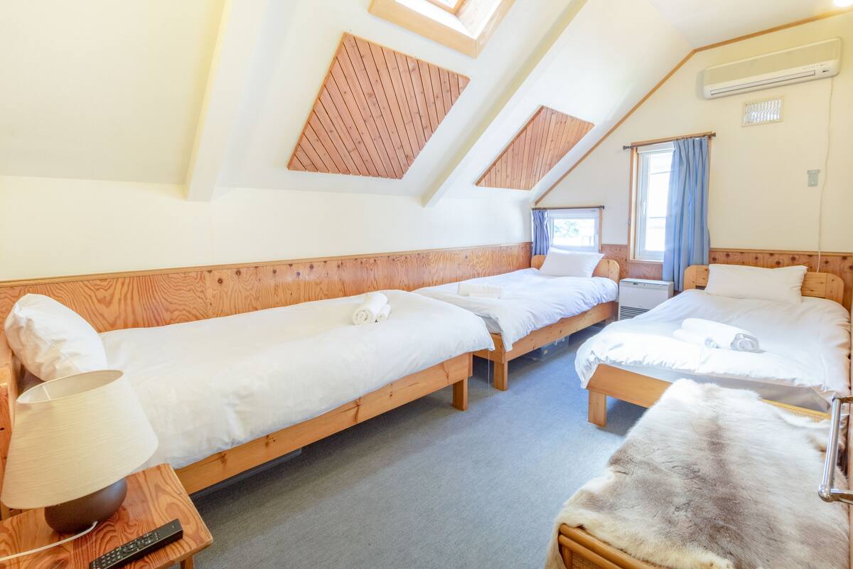 A room with three wooden beds, a lamp, a fur rug, and a remote control on a nightstand.