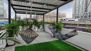 Una terraza en la azotea con hamacas colgantes, plantas en macetas y vistas a la ciudad.