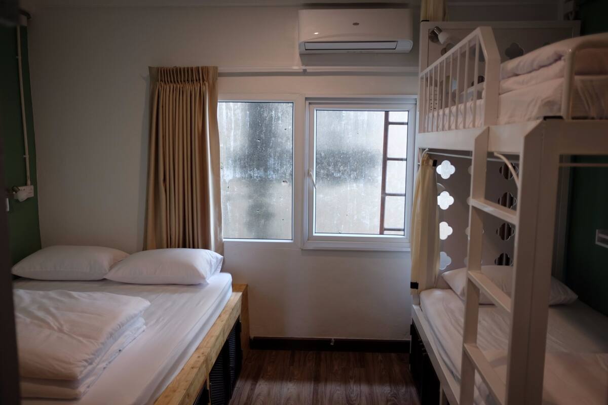 Una habitació amb lliteres, un llit individual, una finestra amb cortines i un aparell d'aire condicionat.