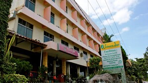 Um hotel de vários andares com um letreiro grande 'TOFFU', uma placa indicando comodidades como quartos com ar condicionado, restaurante, lavanderia e internet.