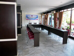 Una sala conferenze con un lungo tavolo e sedie rosse, uno striscione appeso al muro e ampie finestre con tende.
