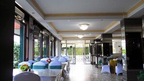 Um restaurante com mesas e cadeiras, piso de mármore e vista para o verde lá fora.