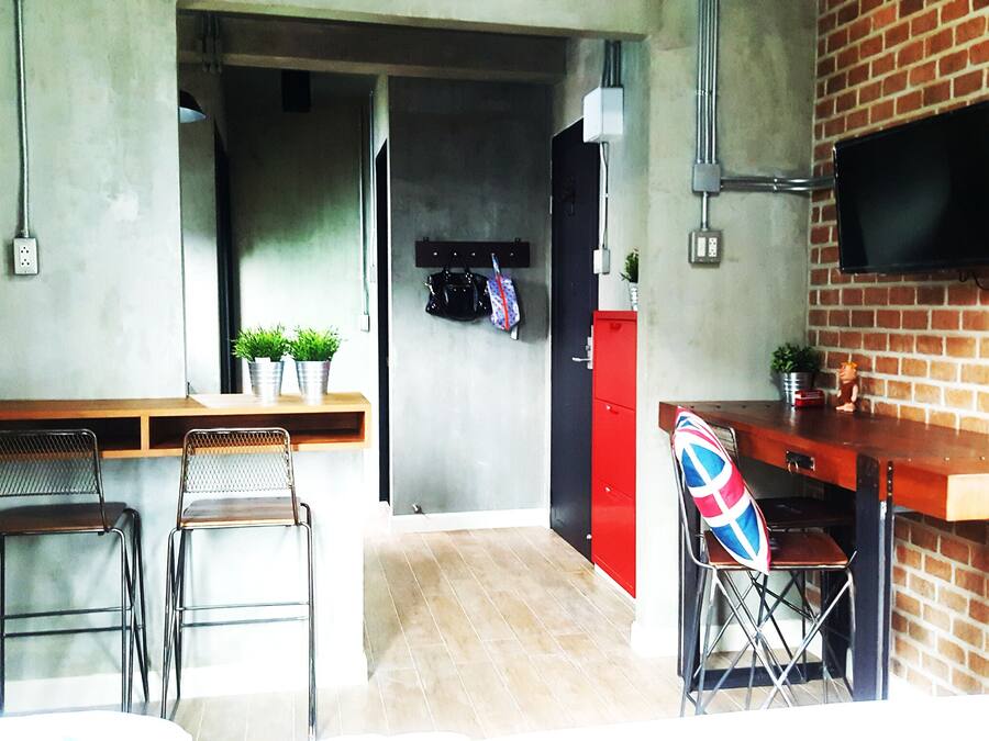 A compact kitchen with a wooden countertop, two metal chairs, a red cabinet, and a TV mounted on a brick wall.