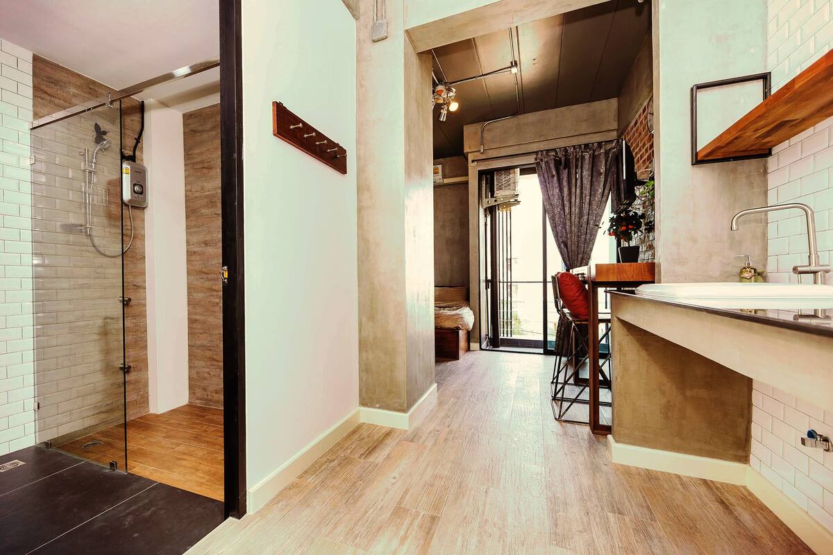 A modern bathroom with a glass shower enclosure, a wooden floor, and a visible towel rack.