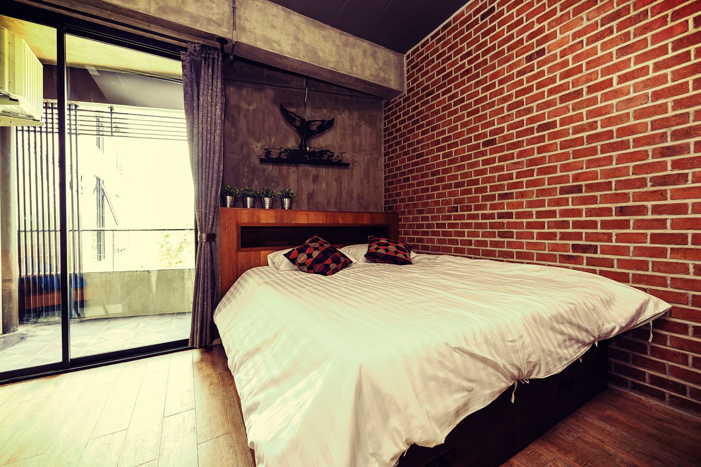 Quarto com uma cama grande, cabeceira de madeira e parede de tijolos.