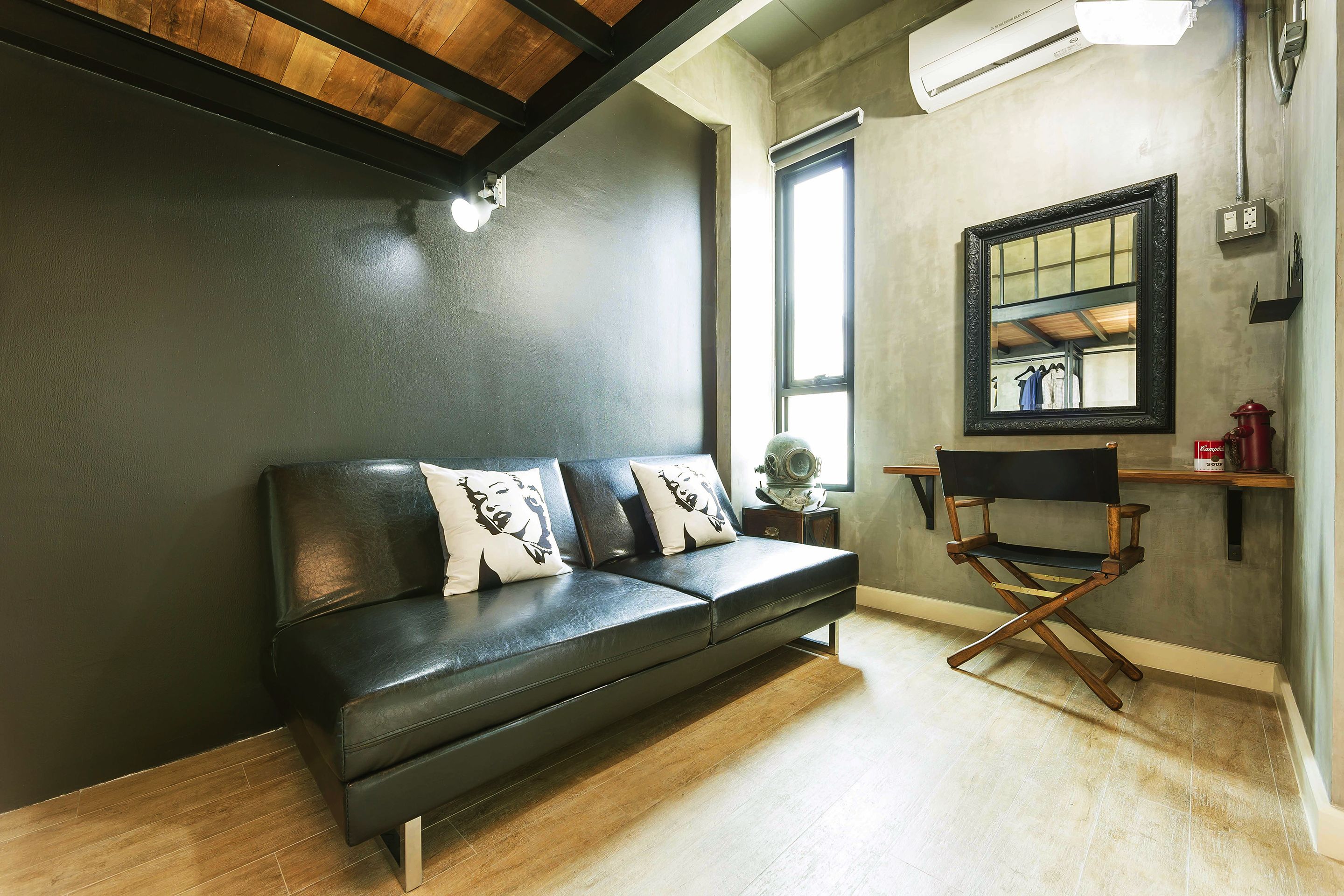 A modern living room with a black leather sofa, a director's chair, and a large mirror on the wall.