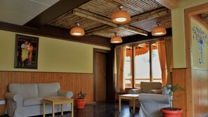 Een kamer met een houten plafond, een bank, een tafel, twee stoelen en potplanten.