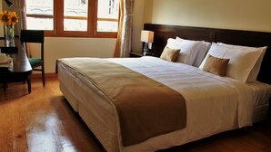 Een hotelkamer met een groot bed, een nachtkastje met een lamp, een stoel en een raam met gordijnen.