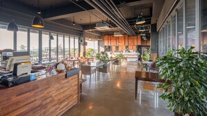 Ein geräumiges Café mit einer Holztheke, moderner Pendelleuchten und großen Fenstern mit Blick ins Freie.