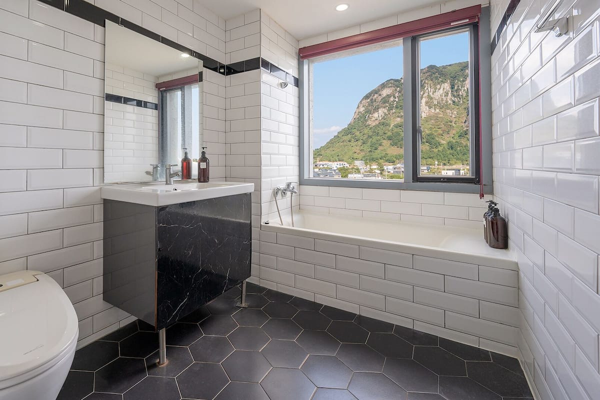 A modern bathroom with white subway tiles, a black marble sink, a white toilet, and a bathtub.