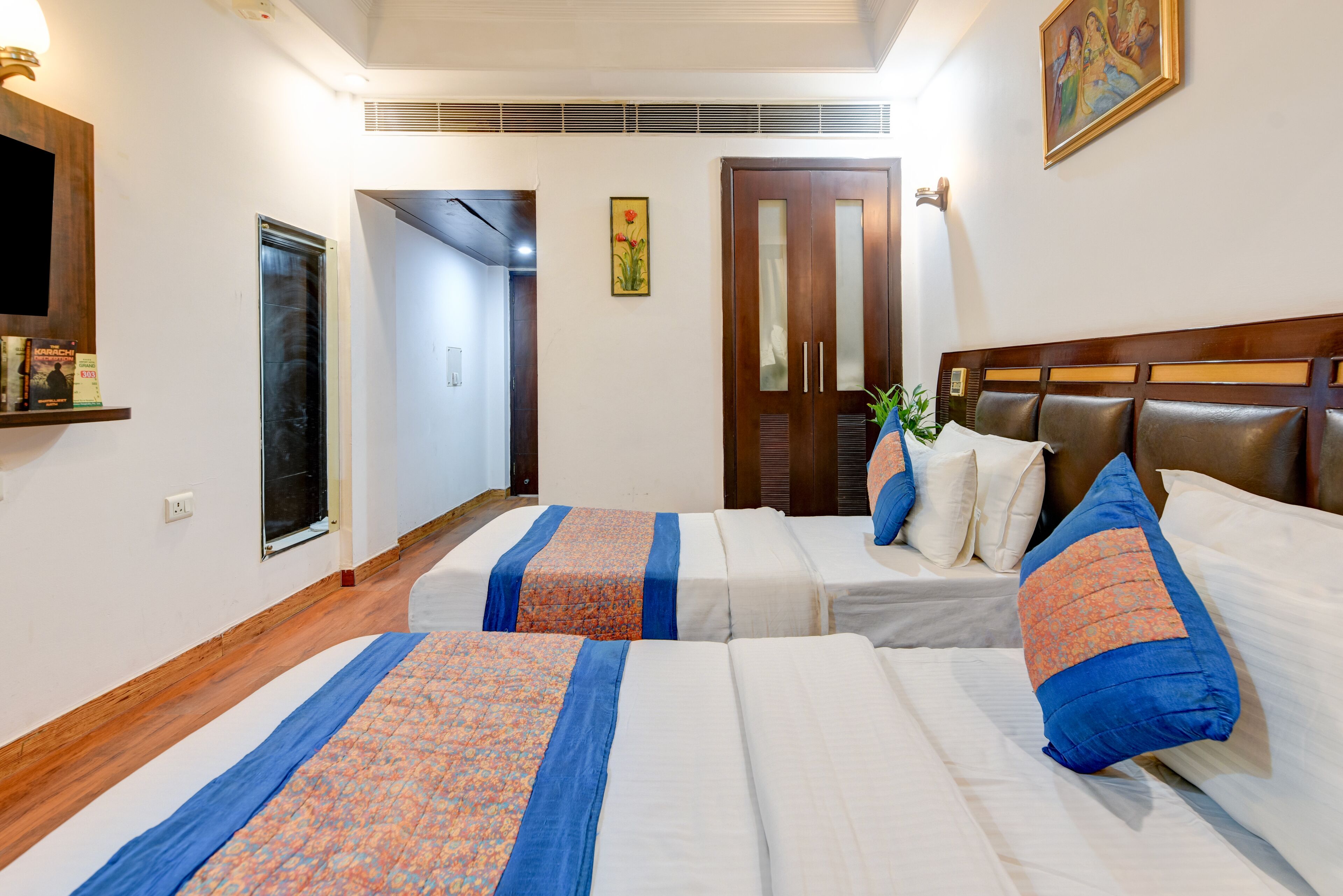 A hotel room with two beds, a wooden headboard, a television, and a door leading to another room.