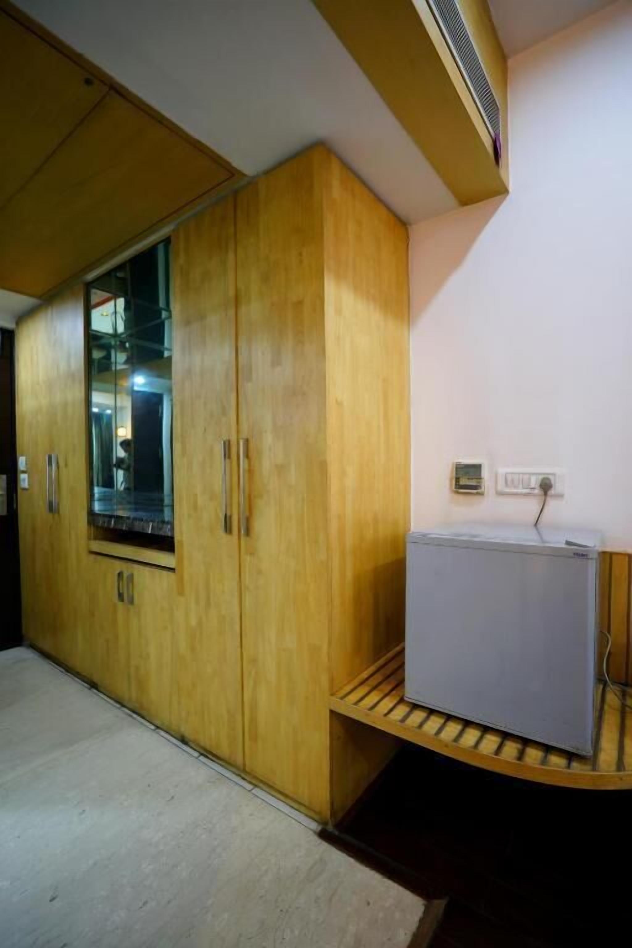A room with wooden wardrobes, a built-in air conditioning unit, and a small refrigerator on a wooden shelf.