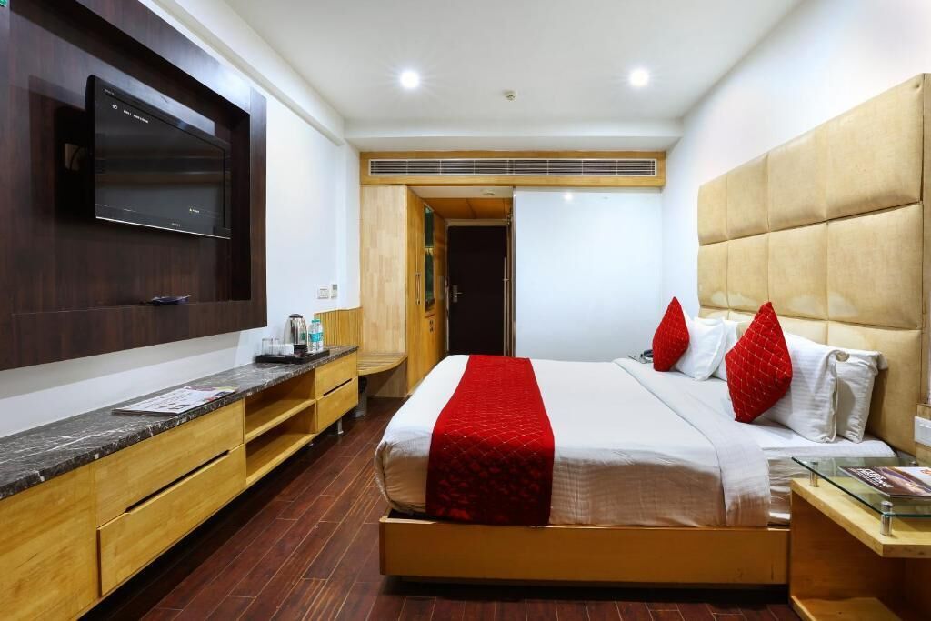Une chambre d’hôtel avec un grand lit, un téléviseur à écran plat fixé au mur, des meubles en bois et une couvre-lit rouge et blanche.