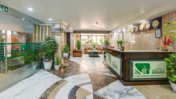Un vestíbulo de hotel con mostrador de recepción, zona de estar y plantas en macetas.